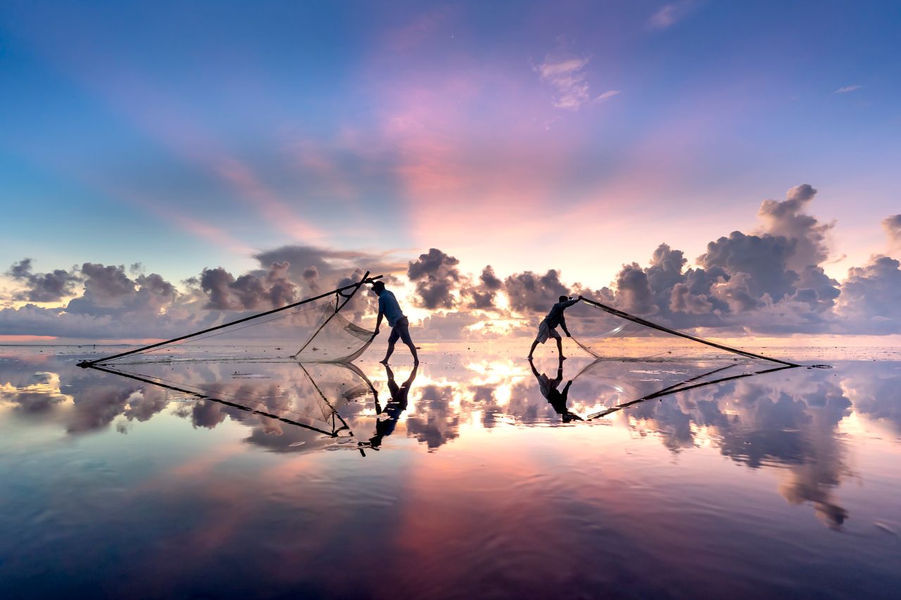 silhouetted fishermen casting nets during a vivid sunset over tranquil