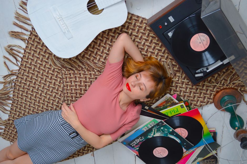 Fotomural Una joven mujer tumbada pacíficamente en una alfombra con discos de vinilo y una guitarra, disfrutando de la música en casa.