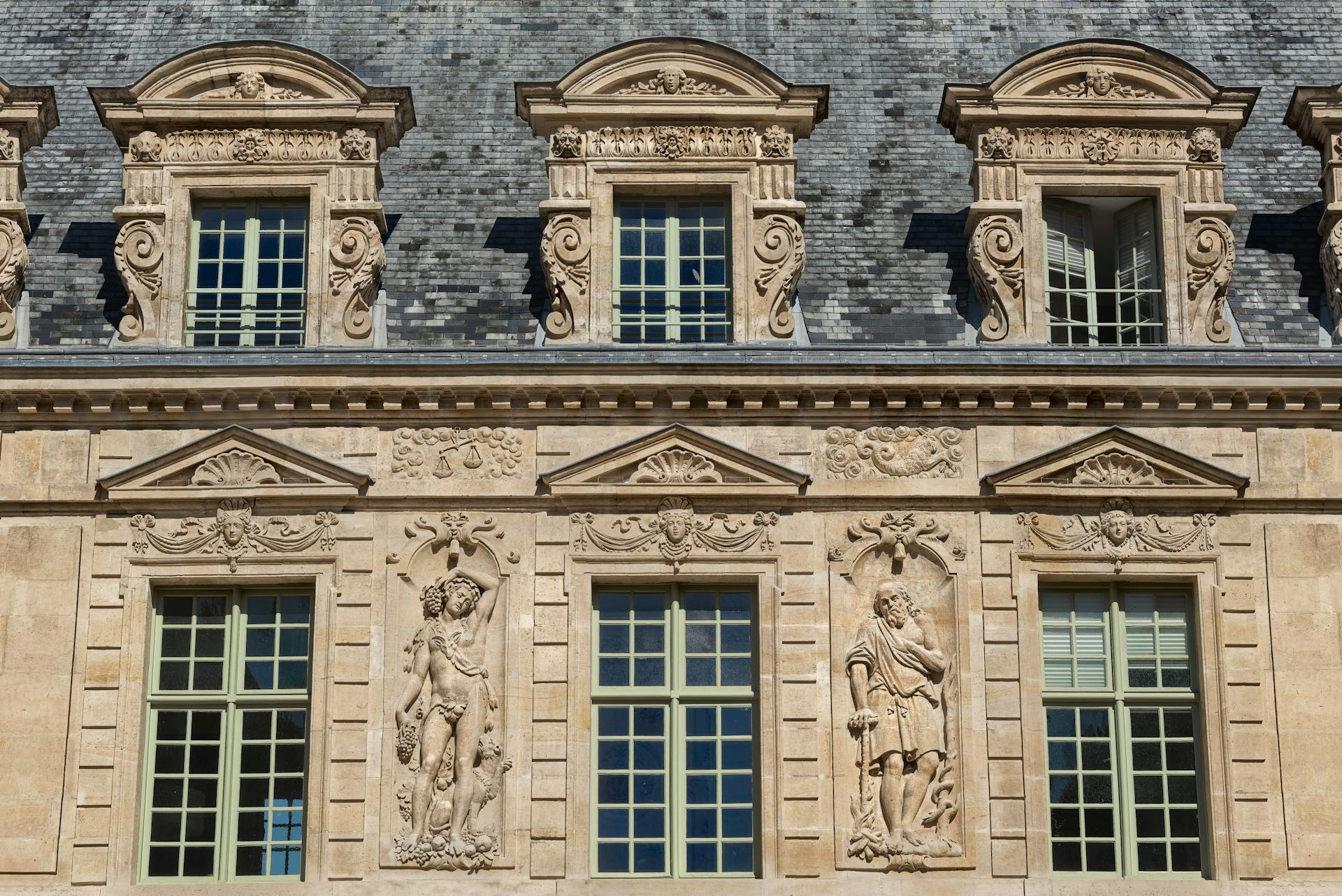 Detailed stone sculptures and windows on a Parisian building facade.