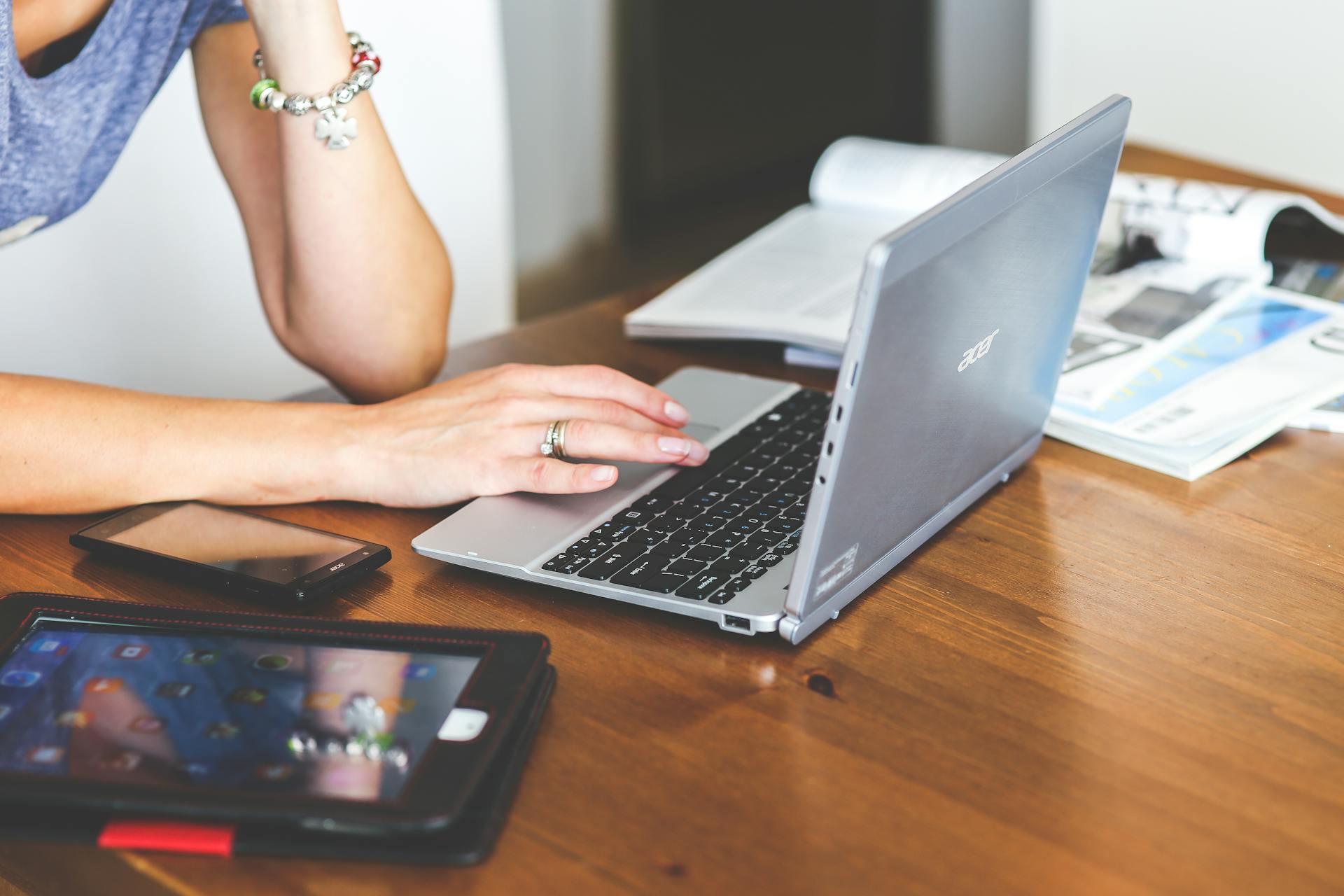 Woman working remotely on a laptop with mobile devices on a wooden desk.