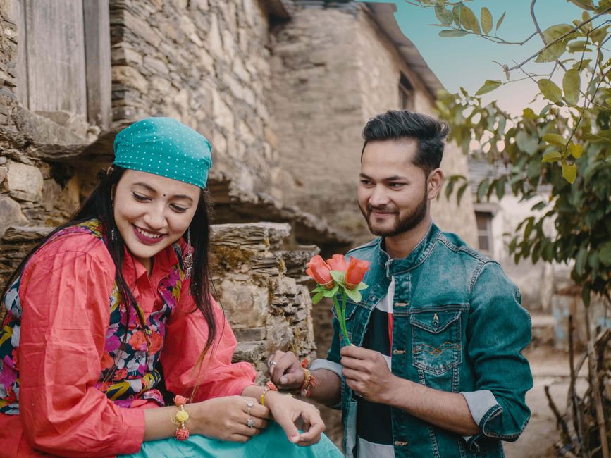 Smiling couple outdoors with flowers, showing affection and joy.
