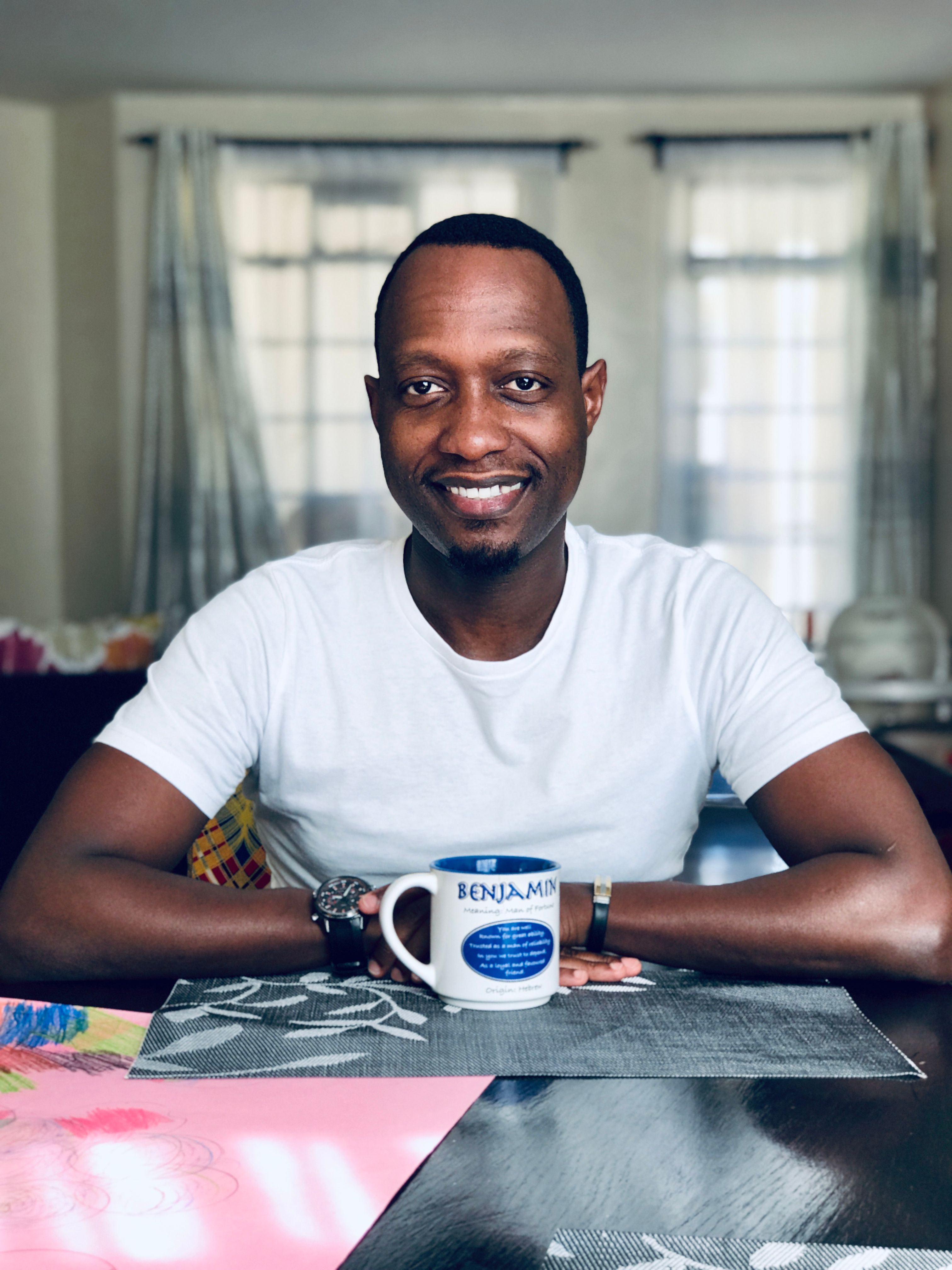 Portrait of a smiling man sitting indoors with a coffee mug in Nairobi, Kenya.
