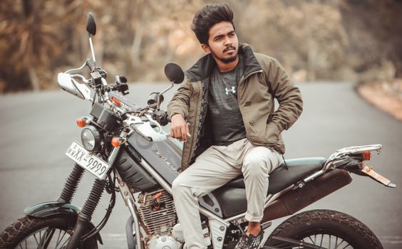 Man sitting on a motorbike parked on a quiet rural road, exuding a relaxed vibe.