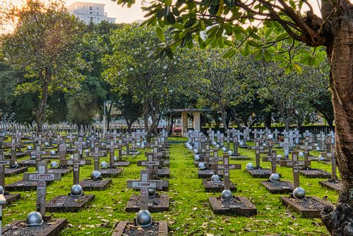 Free Abundance of tombstones with hardhats located on grassy ground in national main heroes cemetery with green trees against tall building Stock Photo