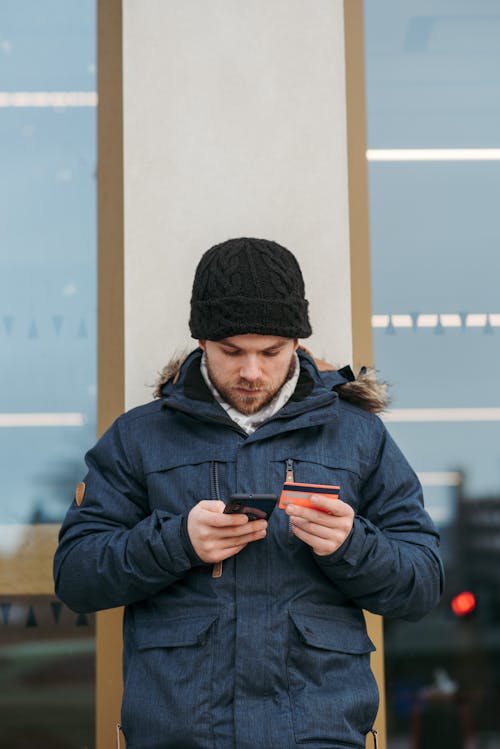 Man In Zwarte Gebreide Muts En Zwarte Jas Met Zwarte Smartphone