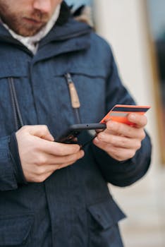 Young man uses smartphone and credit card to make an online purchase outdoors.