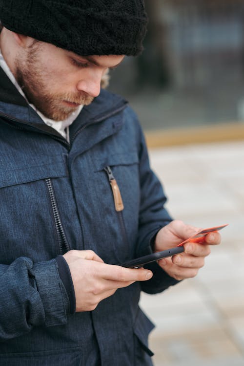 Calm guy standing on street with smartphone while making online payment with credit card