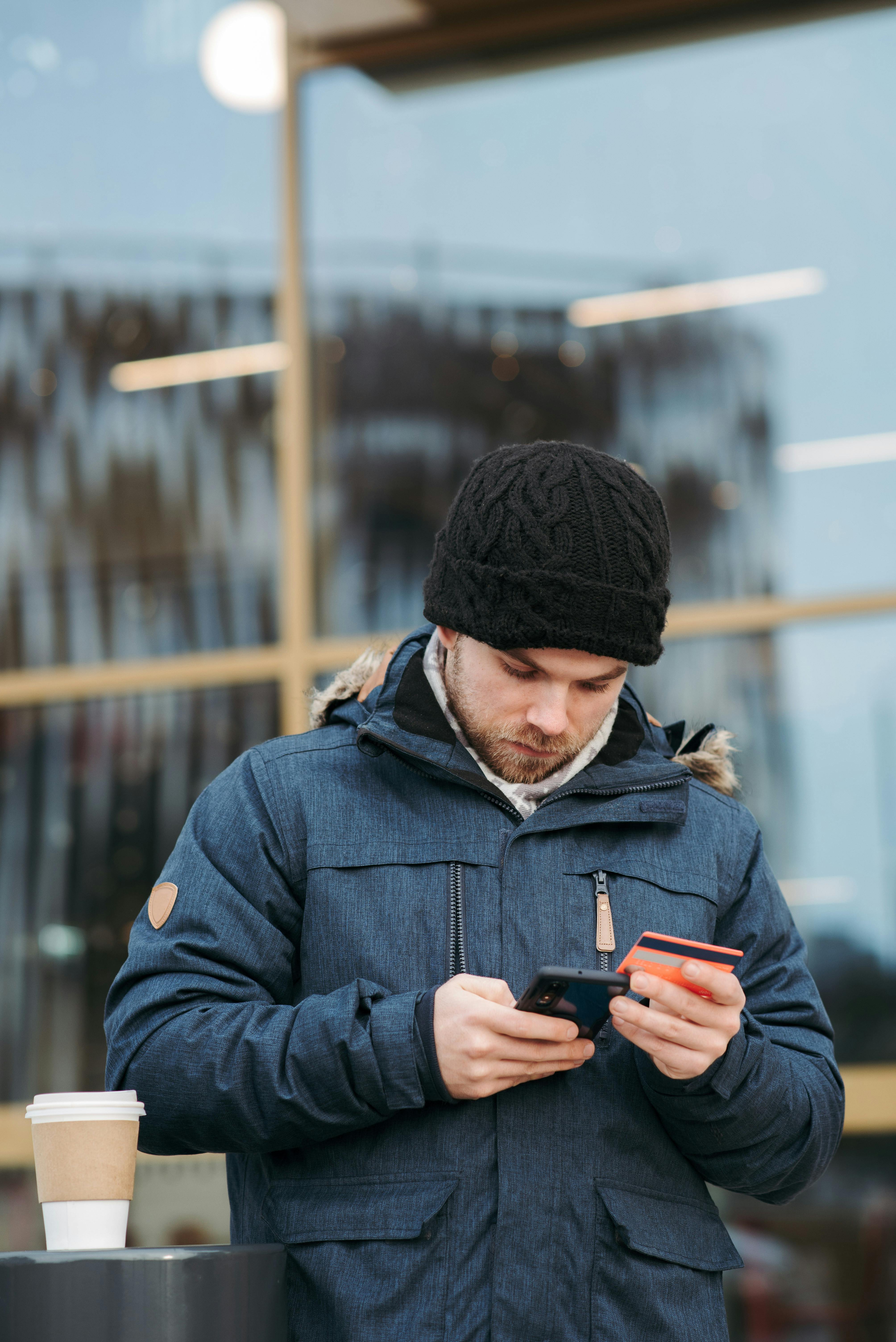 serious man using plastic card while making online shopping on smartphone on street