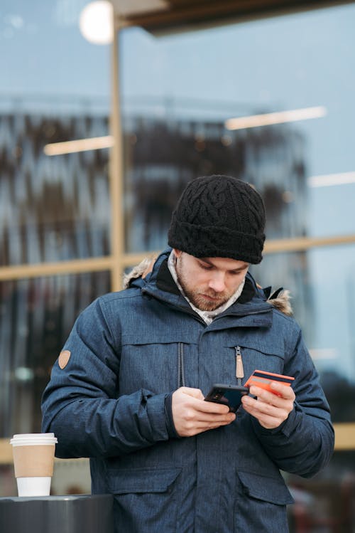Serious man using plastic card while making online shopping on smartphone on street