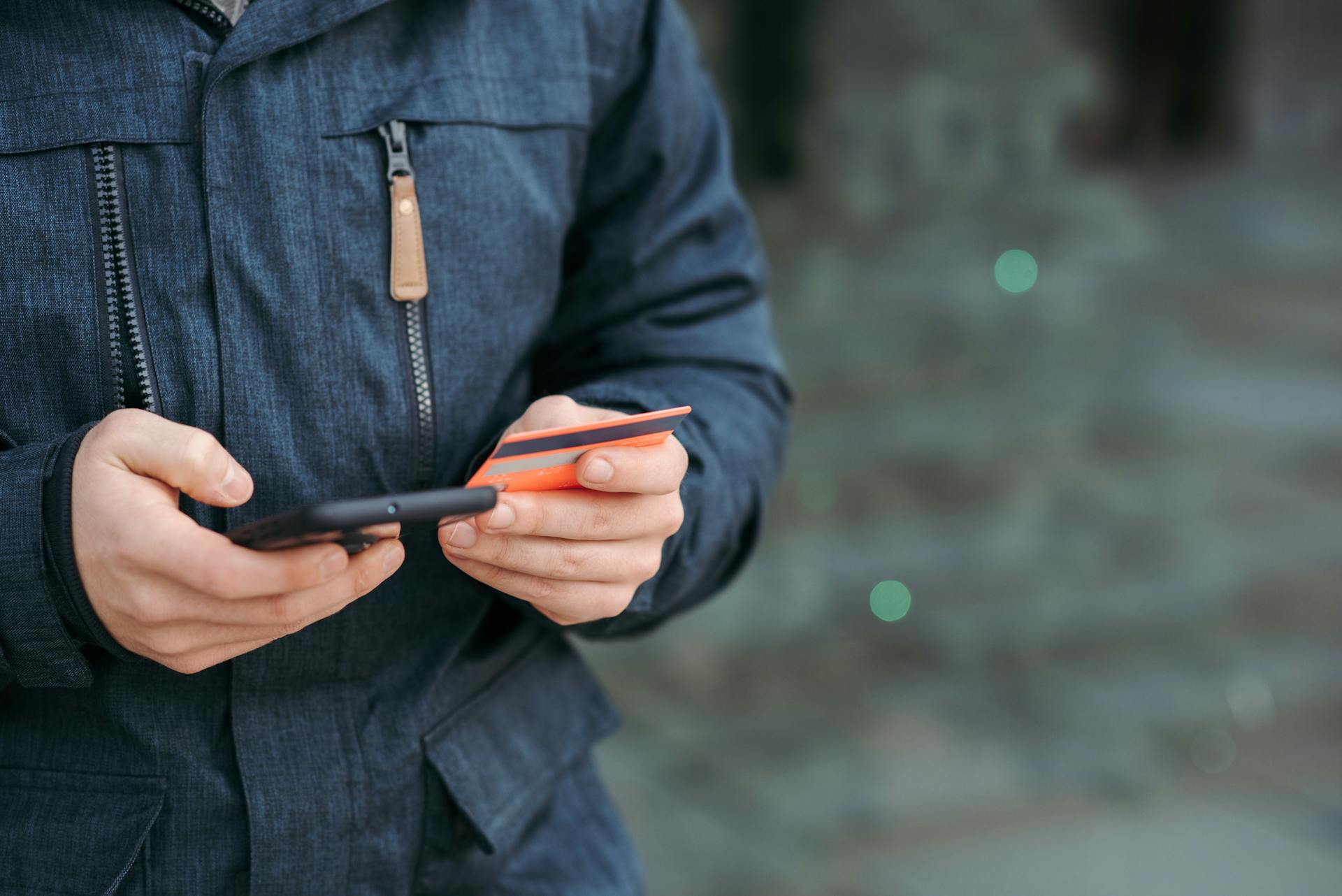 Close-up of a person making an online purchase with a smartphone and credit card outdoors.