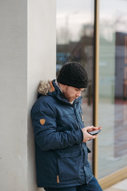 Homme En Veste Bleue Et Bonnet En Tricot Noir à L'aide De Smartphone