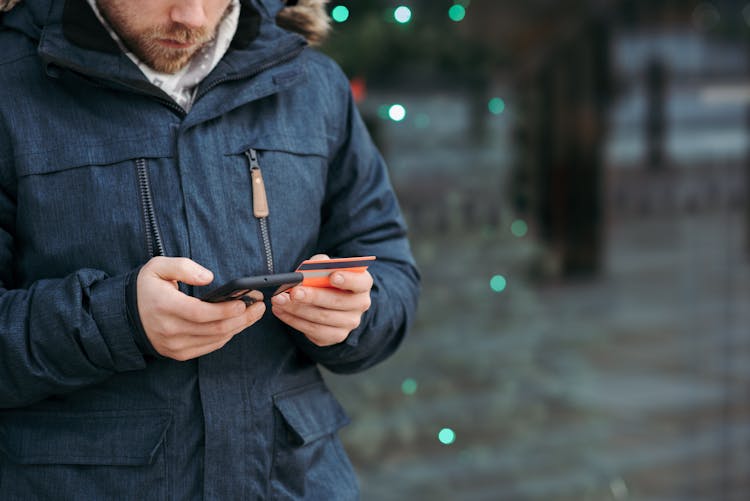 Man Browsing Smartphone And Holding Credit Card On Street