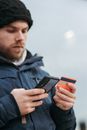 Crop man in warm clothes entering details of credit card on mobile phone while making online purchases on street in daytime