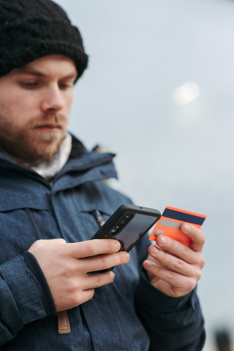 Focused Male In Outwear Typing Credentials Of Credit Card On Smartphone