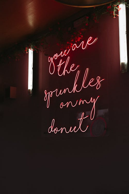 Red neon signboard with inscription hanging on wall in dark public place at night