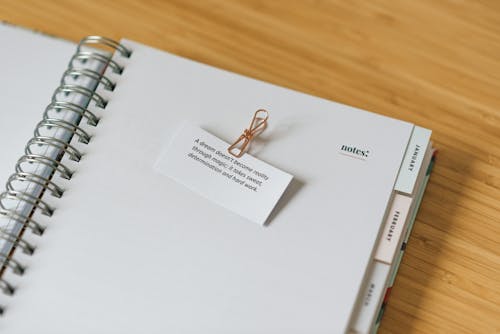 Free High angle of open spiral notebook with message and clip on white paper sheet on wooden table Stock Photo