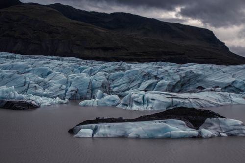 Free A breathtaking view of a glacier amidst dark mountains and cloudy skies, showcasing natural beauty. Stock Photo