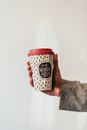 Crop anonymous person showing paper cup of hot beverage to go with ornament and inscription