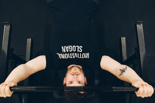 Bearded sportsman in t shirt with inscription exercising with weight while looking at camera