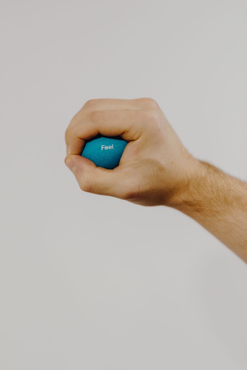 O que são fidgets sensoriais e para que servem? Mão segurando uma bola de squeeze azul para alívio do estresse e regulação sensorial
