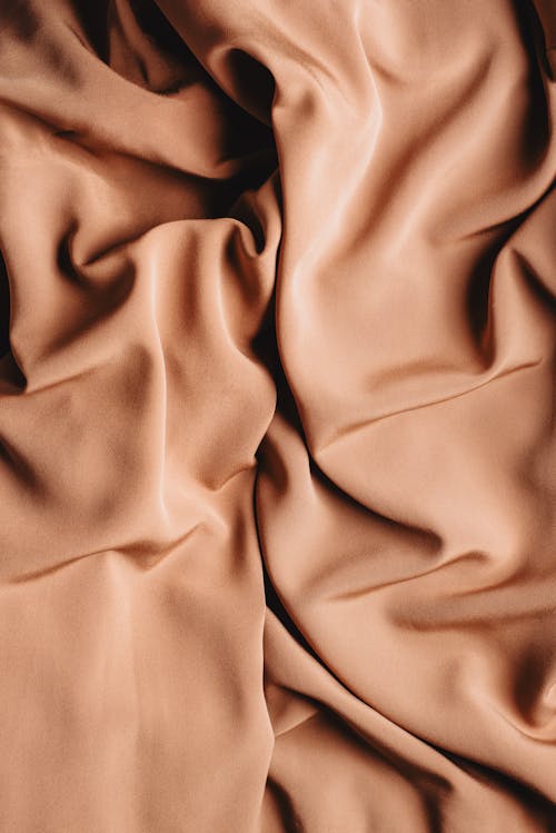Overhead view of background representing creased beige fabric with silky surface and soft texture