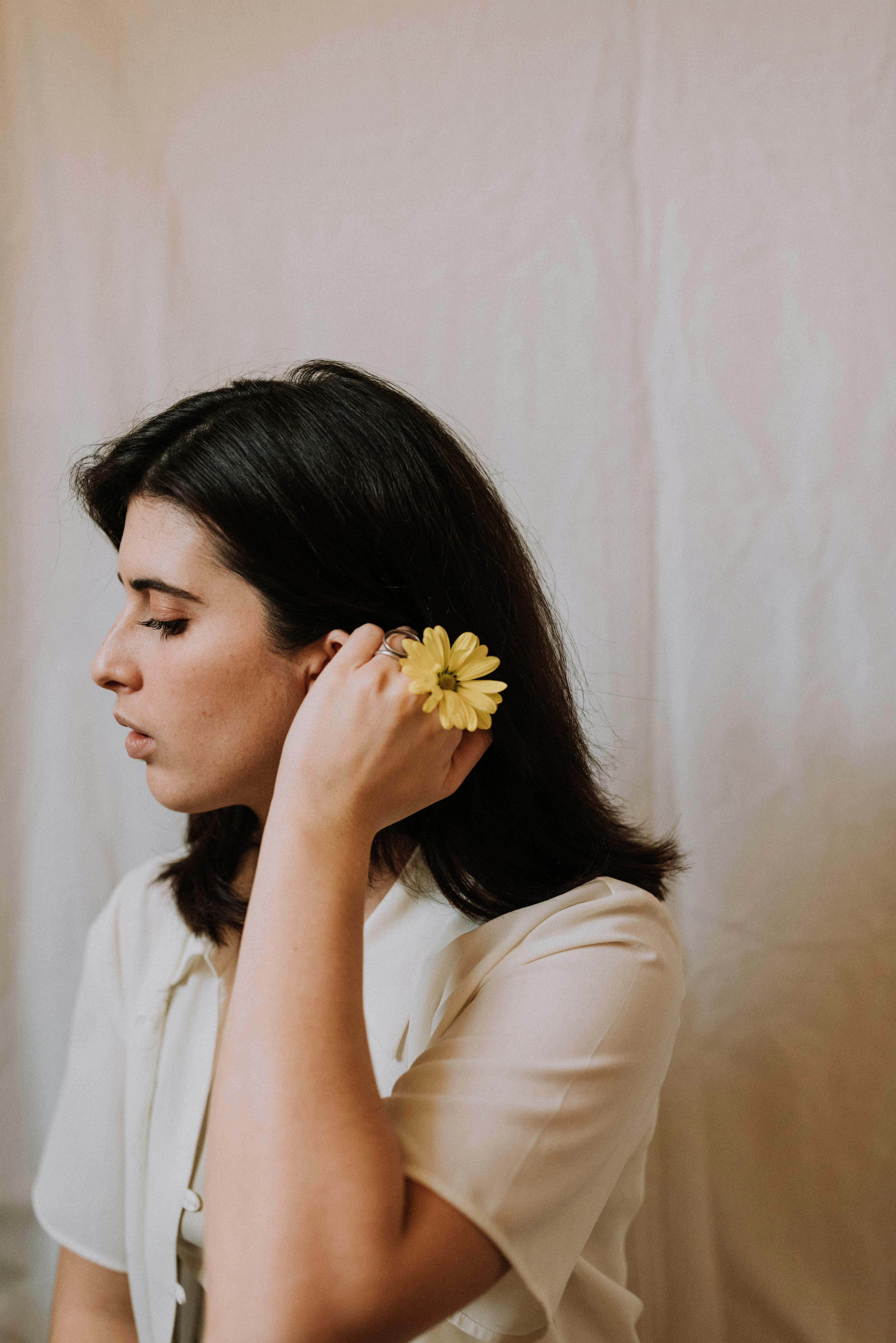 Adult gentle ethnic female with makeup and blossoming yellow flower with pleasant aroma looking down