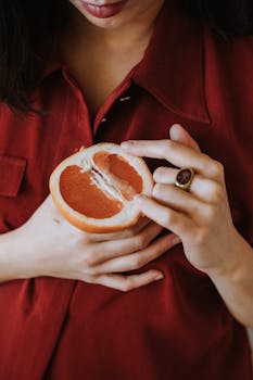 Close-up of a woman in a red blouse holding a juicy half grapefruit, emphasizing freshness and health.