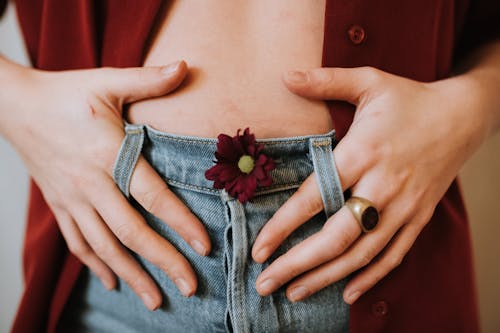 Free Crop faceless female in casual clothes decorated with blooming flower revealing bare stomach Stock Photo