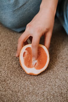 A close-up image of a hand holding a juicy grapefruit half on a carpeted floor.