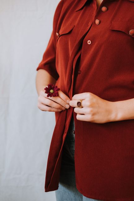 Crop unrecognizable female with blooming decorative flower and ring on fingers buttoning shirt