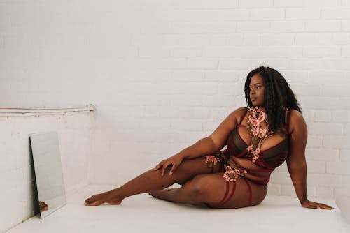 Free Full body of gorgeous barefoot overweight African American female in underwear leaning on floor and looking at reflection in mirror Stock Photo