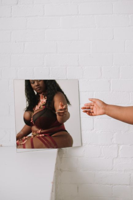 Elegant black woman in fashionable attire reflected in a mirror, showcasing individuality.
