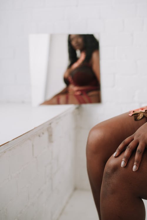 Crop unrecognizable black woman in bodysuit touching breast against mirror  · Free Stock Photo