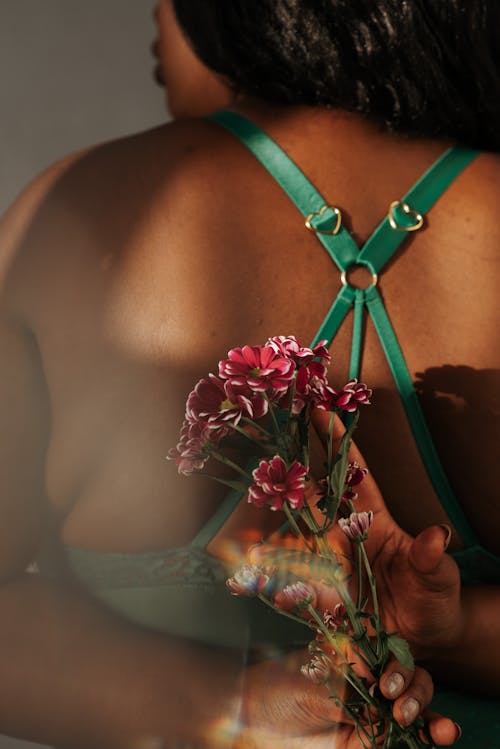 Free Back view crop faceless African American female in lingerie showing delicate pink flowers behind back Stock Photo