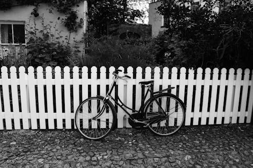 Free Grayscale Photo of Bicycle near White Wooden Fence Stock Photo
