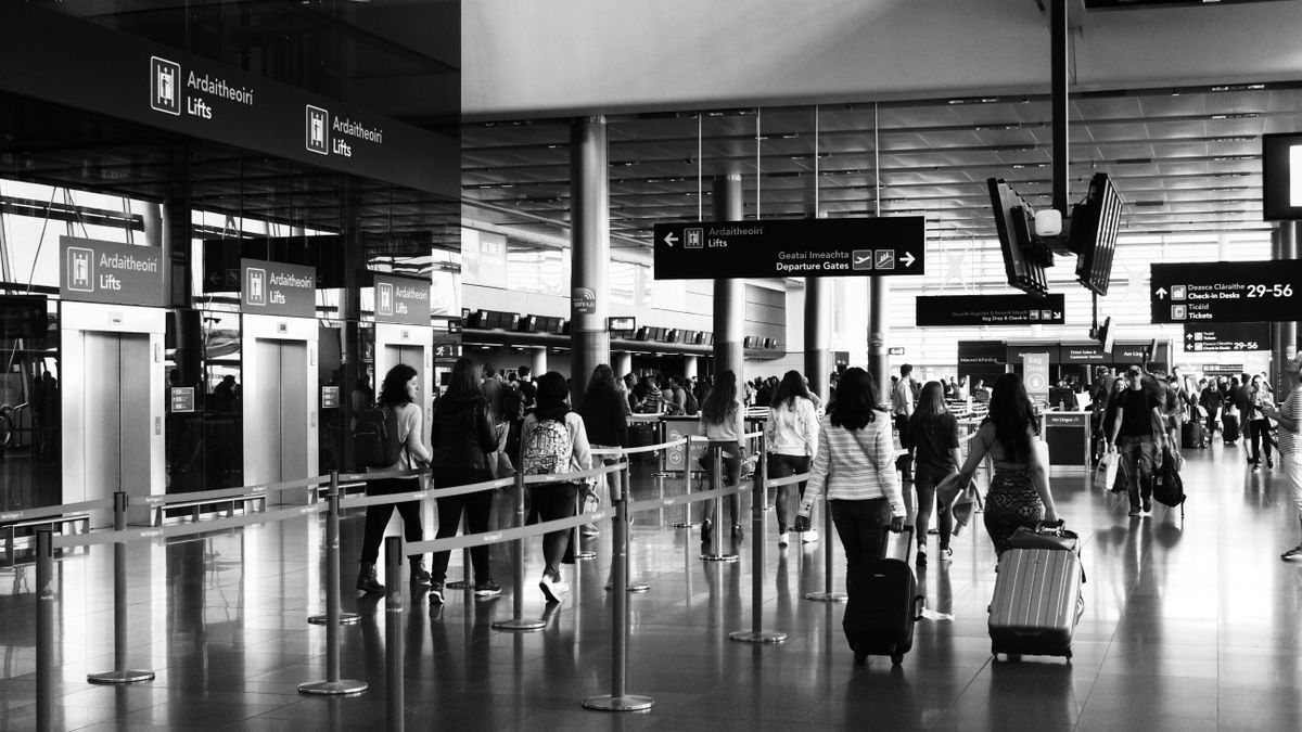 Black and white photo of travelers walking with luggage in a bustling airport terminal.