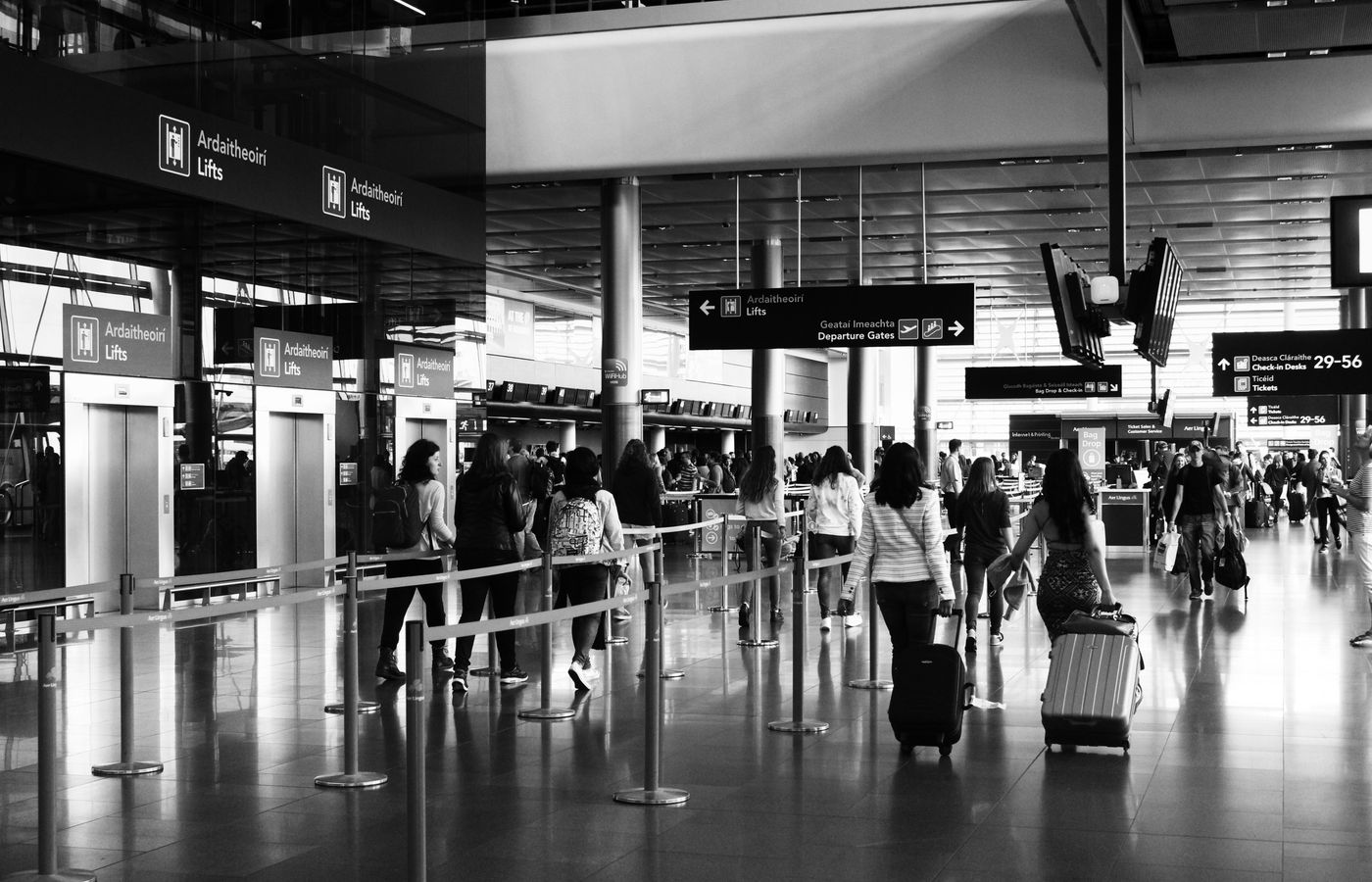 Black and white photo of travelers walking with luggage in a bustling airport terminal.