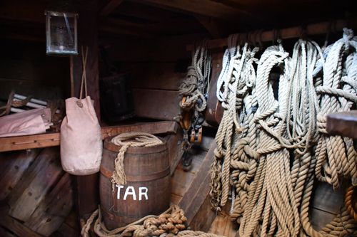 Free Vintage ship interior showing a wooden barrel labeled 'TAR' surrounded by coiled ropes and rustic decor. Stock Photo