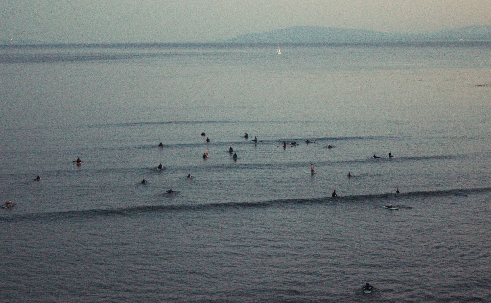 Surfers gather in the ocean at twilight, waiting for the perfect wave