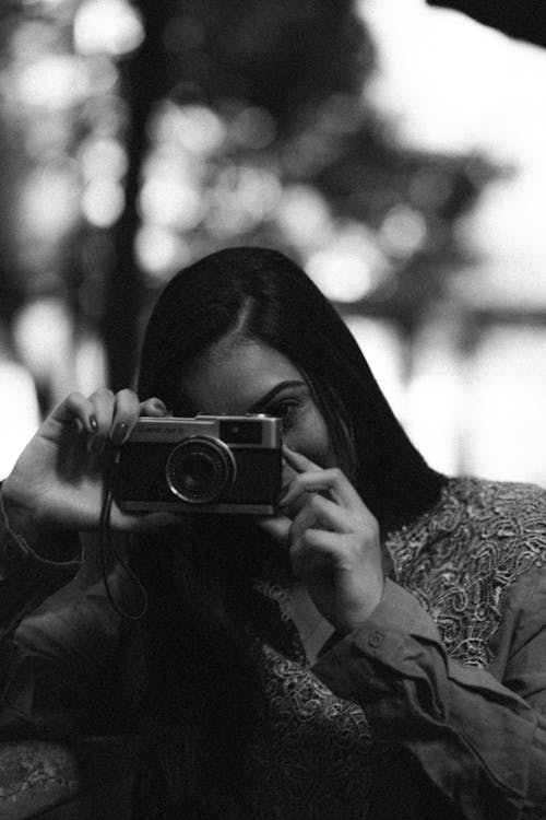 Free Black and white of unrecognizable female photographer taking picture with retro photo camera in park with trees on blurred background Stock Photo