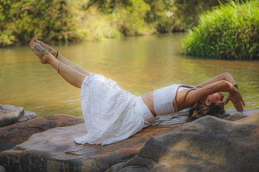 Full body side view of active female in white wear balancing on stone while practicing yoga near calm lake in nature