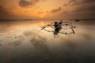 宁静的场景，日出时平静的水面上有一艘传统船只，营造出一种宁静而反思的氛围