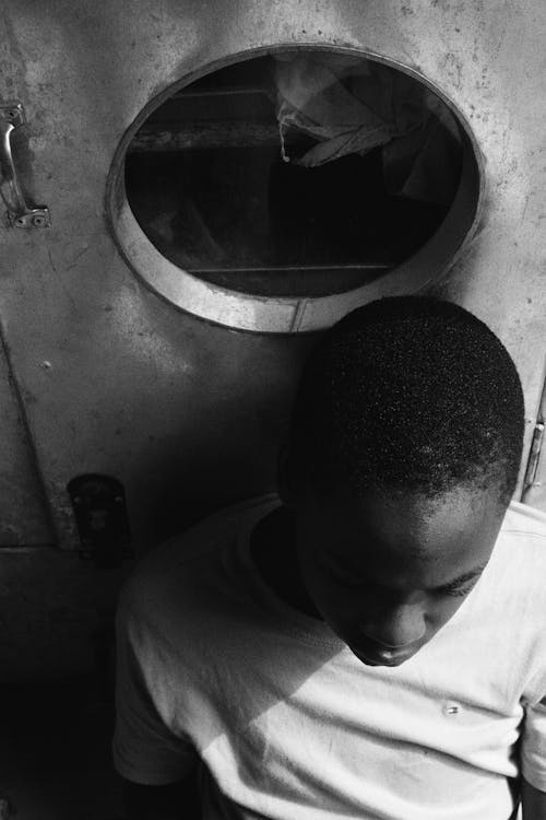 Black and white of focused African American male in casual clothes sitting on floor and leaning on metal door