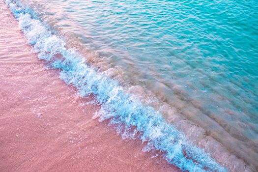 Aerial view of turquoise waves gently crashing on a sandy beach with vibrant colors.