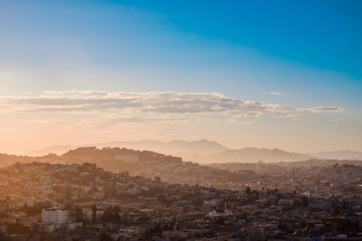 A stunning aerial view of San Francisco at sunset, showcasing urban sprawl with hills and skyline under an orange and blue sky.
