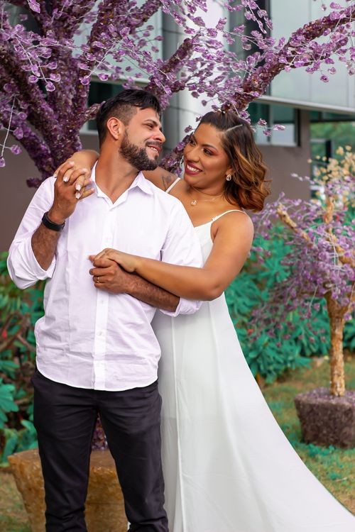 Free Positive ethnic couple in wedding outfits embracing and looking at each other while standing near blooming tree on street in city during holiday celebration Stock Photo