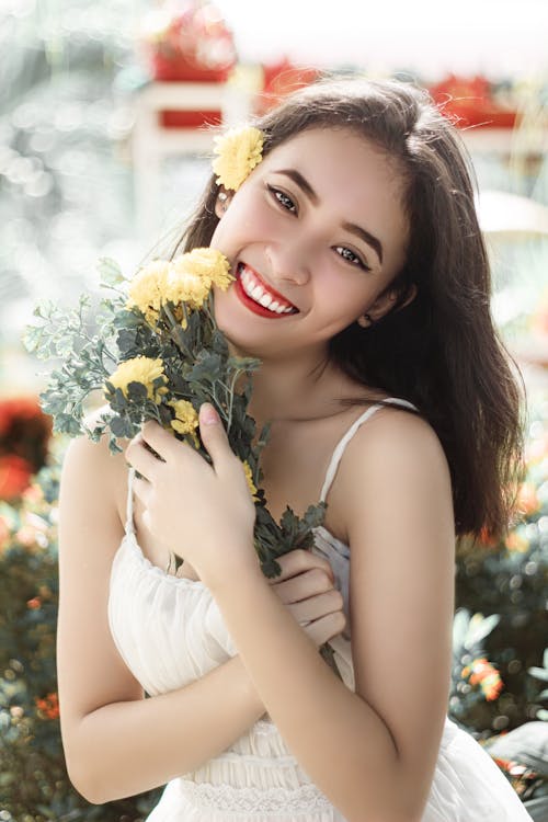 Free Woman in White Dress Holding Yellow Flowers with Green Leaves Stock Photo