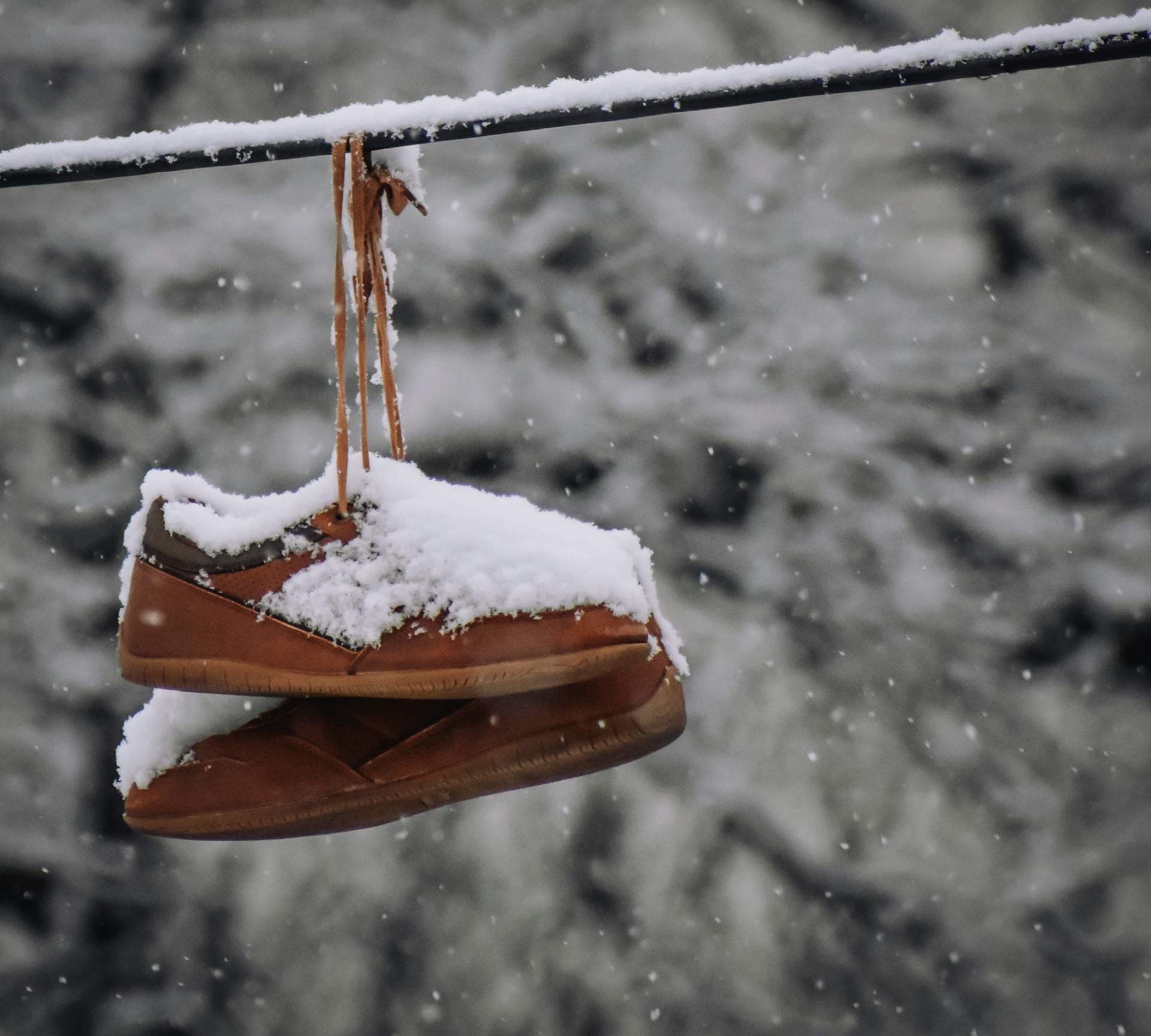 Brown old fashioned footwear covered with snow hanging on rope against leafless trees on blurred background on cold winter day