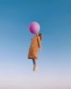 Side view of woman wearing trendy clothes with trench coat flying in sky and blowing enormous balloon