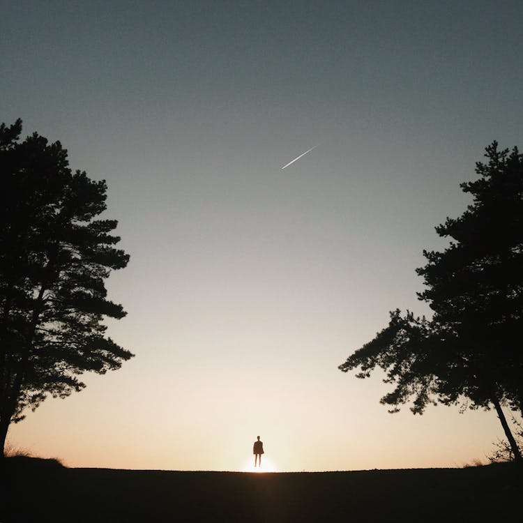 Small silhouette of unrecognizable person looking up on falling star in twilight sky